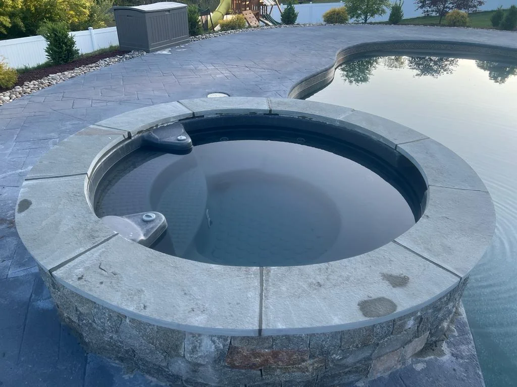 Circular stone spa integrated into a poolside hardscape